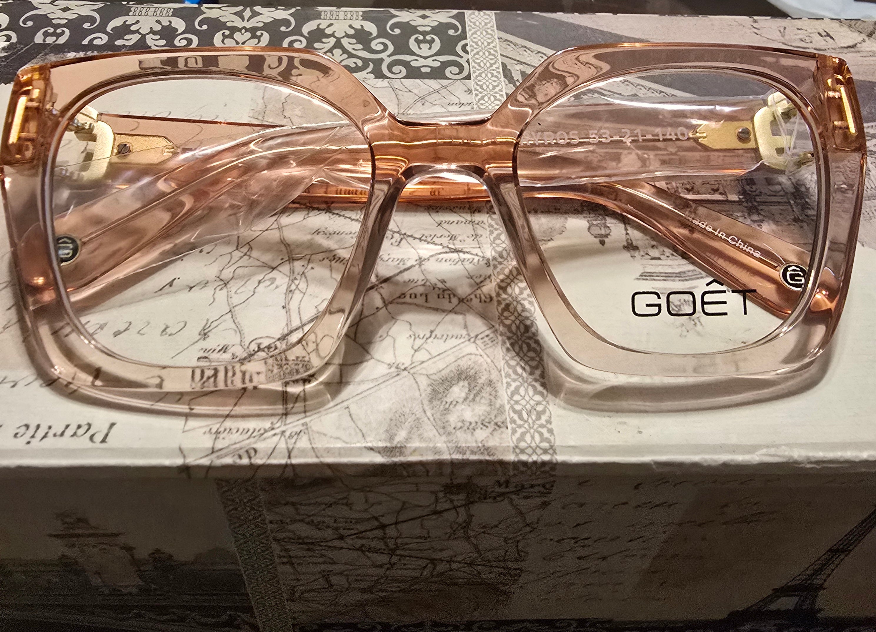 Rose gold eyeglasses with 'GOET' branding on a textured surface